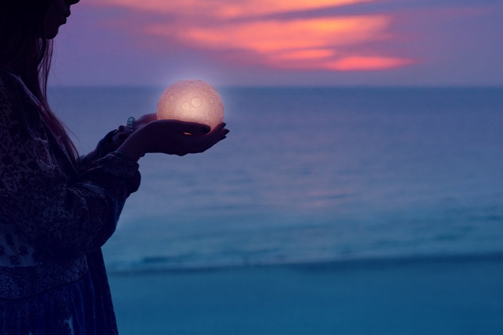 Woman hands holding the sun at dawn.spirituality concept. Image of a woman holding the moon, used to represent Soul Purpose Activation through astrology and energetic strategy