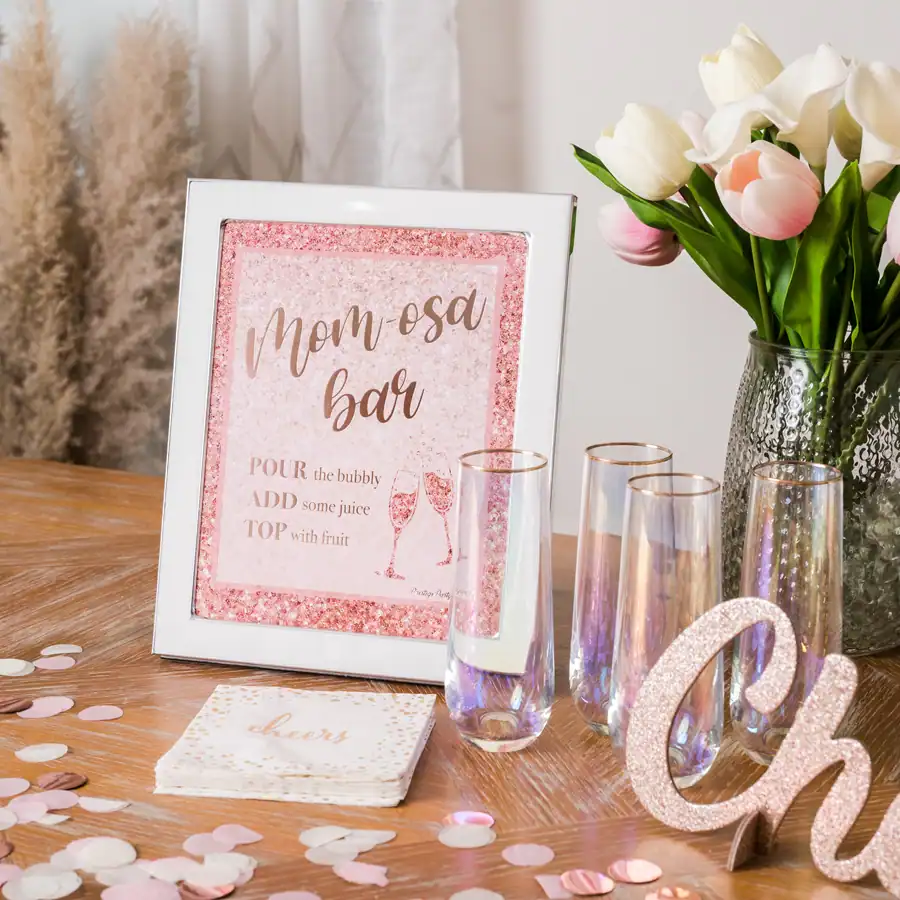 Mom-osa Bar baby shower setup with pink signage, glasses, flowers, and styled confetti—showing lifestyle product photography for Amazon listings.
