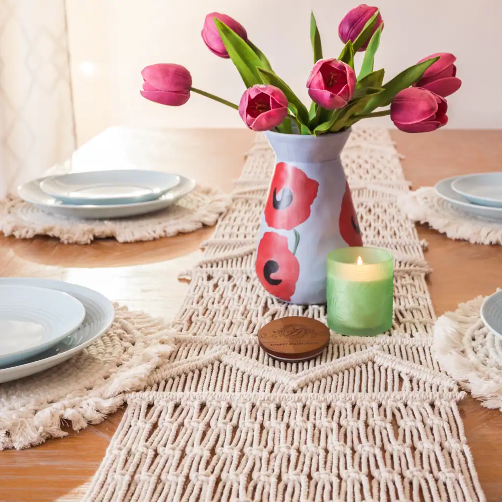interior photography of a dining table with florals and macrame runner and placements with a candle and light blue coastal ceramic plates in warm palm beach style