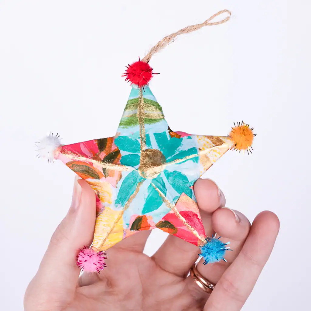 Colorful star ornament with bright floral patterns and pom poms, whimsical hand painted holiday decoration, unique artisan gift.