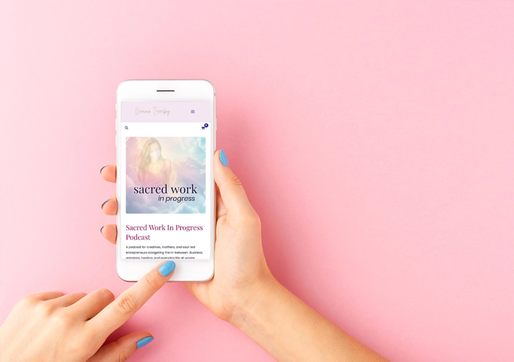 sacred work in progress podcast on mobile device in a womans hand on a light pink background