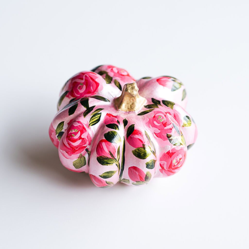Hand-painted pumpkin with pink roses and green leaves on a white background.