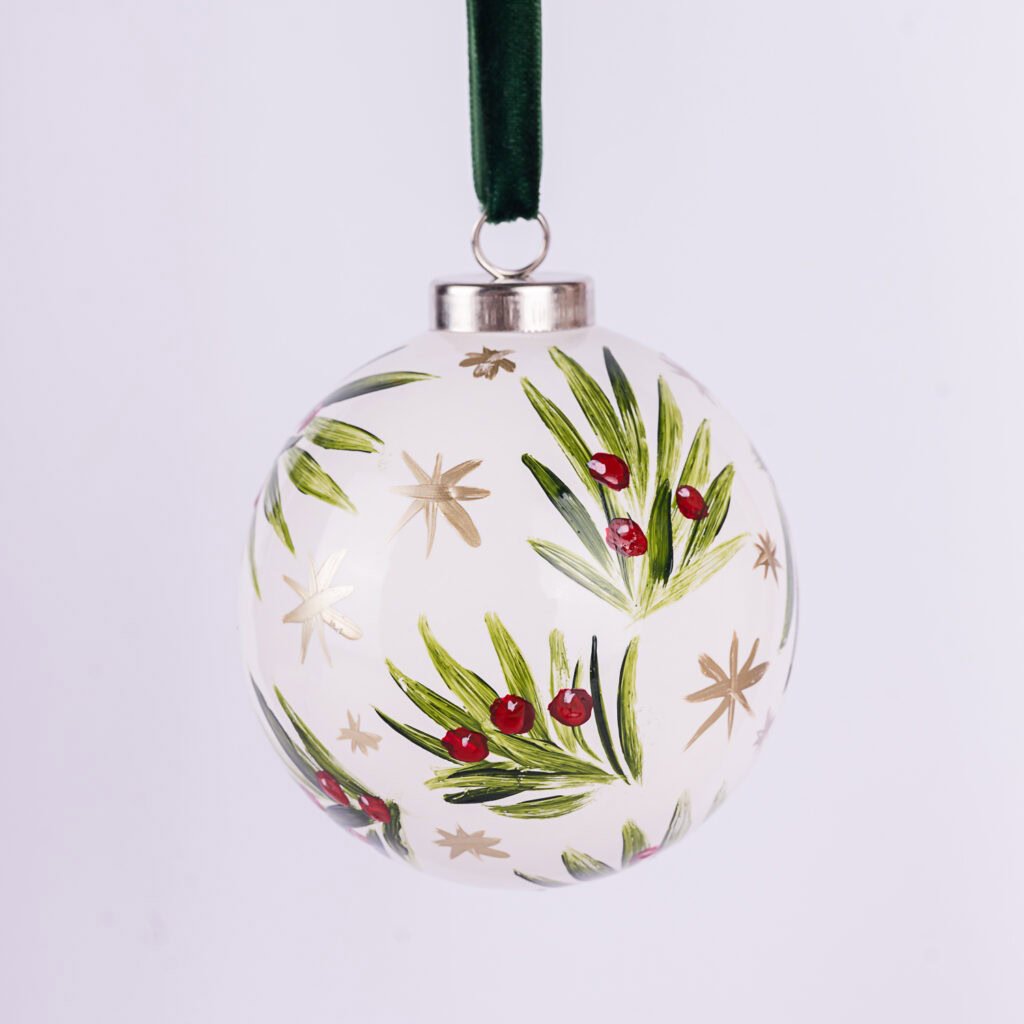 Hand-painted glass ornament with green leaves and red berries, decorated with gold stars, hanging from a green ribbon.