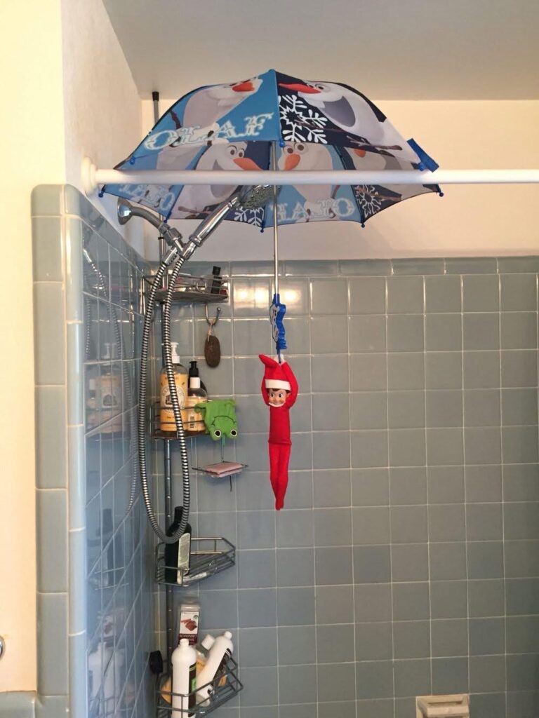 Elf on the Shelf hanging from a kids’ umbrella in the shower like a zip-line. Quick and funny elf idea.