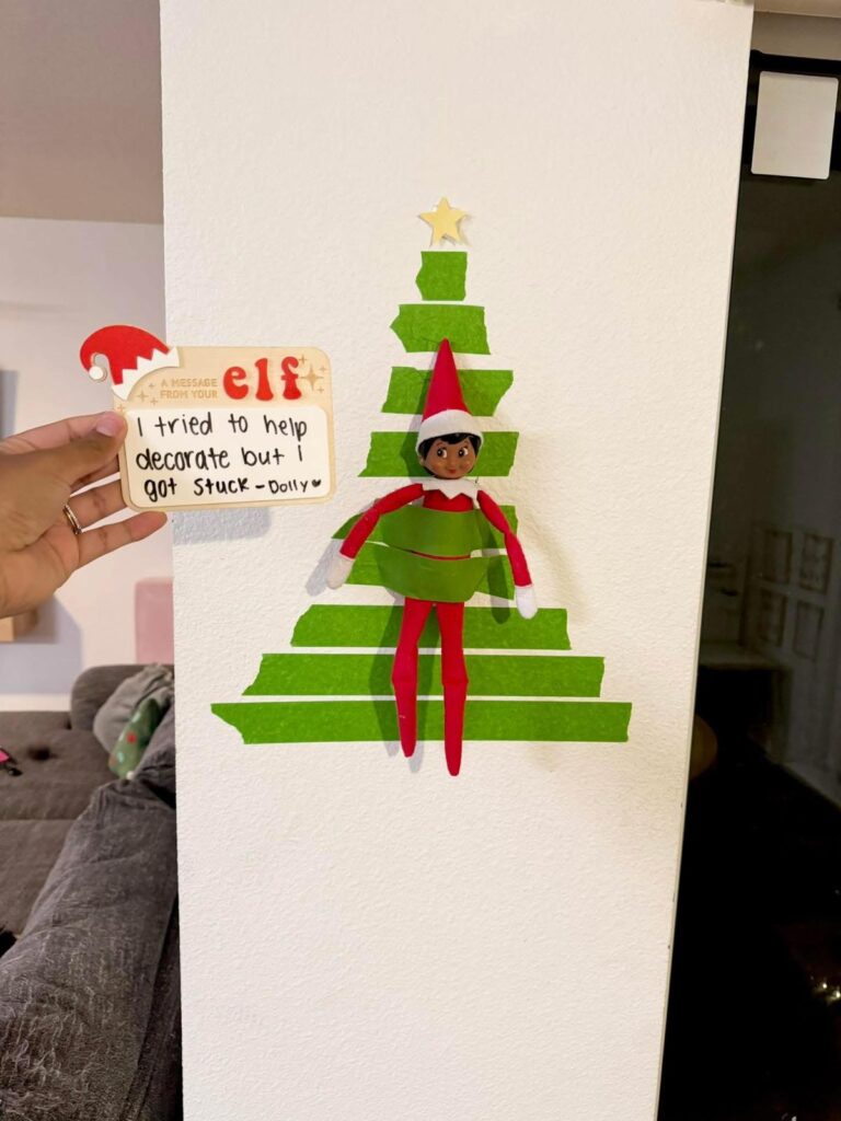 Elf on the Shelf stuck inside a painter’s tape Christmas tree with a funny note. Easy last-minute elf idea for kids.