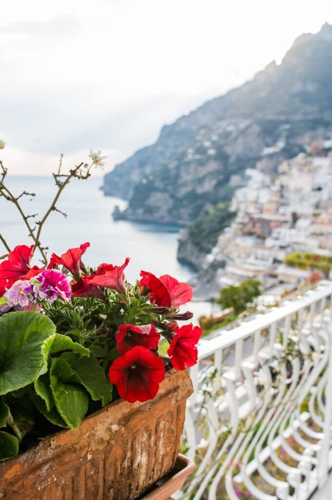 Beautiful red and pink flowers in a terracotta pot with a scenic Positano Amalfi Coast view in the background.
