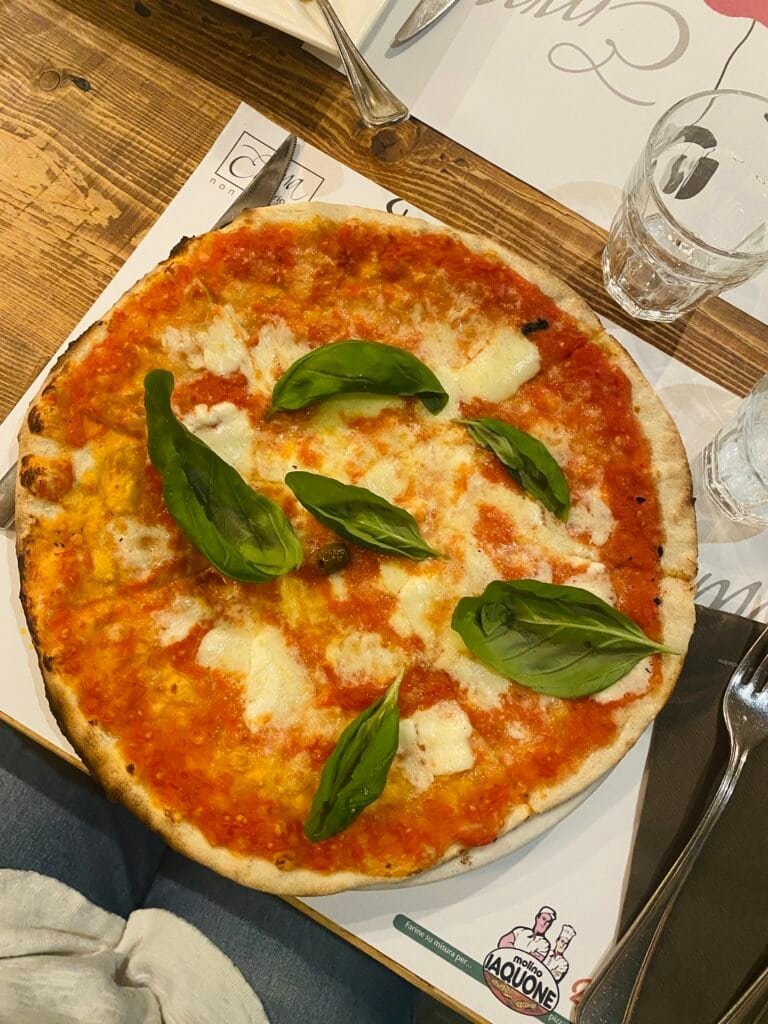 A classic Italian Margherita pizza topped with fresh basil leaves, mozzarella, and tomato sauce, served hot on a wooden table.