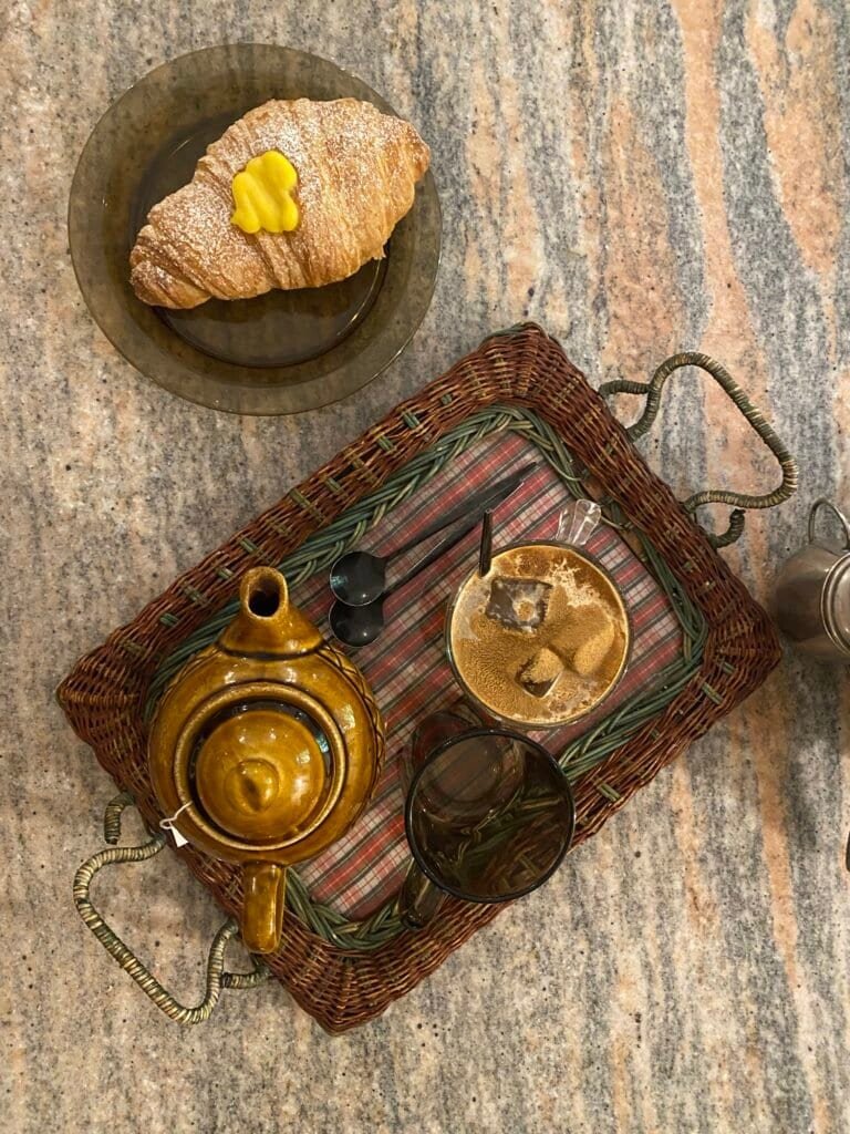 A cozy tea scene featuring a teapot, glass, and a small pastry on a wooden plate, perfect for relaxing moments.