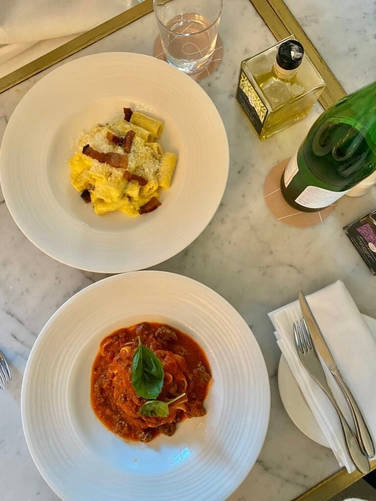 A beautifully presented Italian meal featuring two pasta dishes, one with creamy sauce and bacon, and the other with rich tomato sauce and fresh basil, served on elegant white plates.
