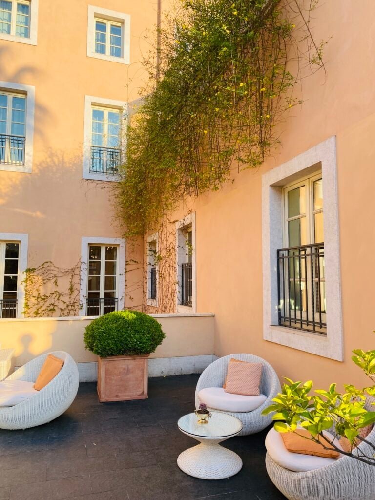 Charming outdoor courtyard with lush greenery, modern seating, and pastel-colored building facades, capturing a serene moment in Italy.