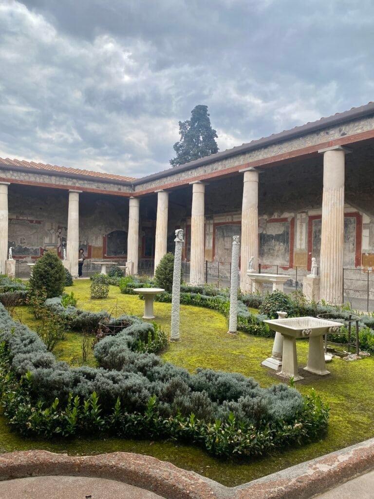A serene view of a historic Roman garden featuring classical columns, lush greenery, and stone sculptures, capturing Italy's rich cultural heritage and timeless beauty.