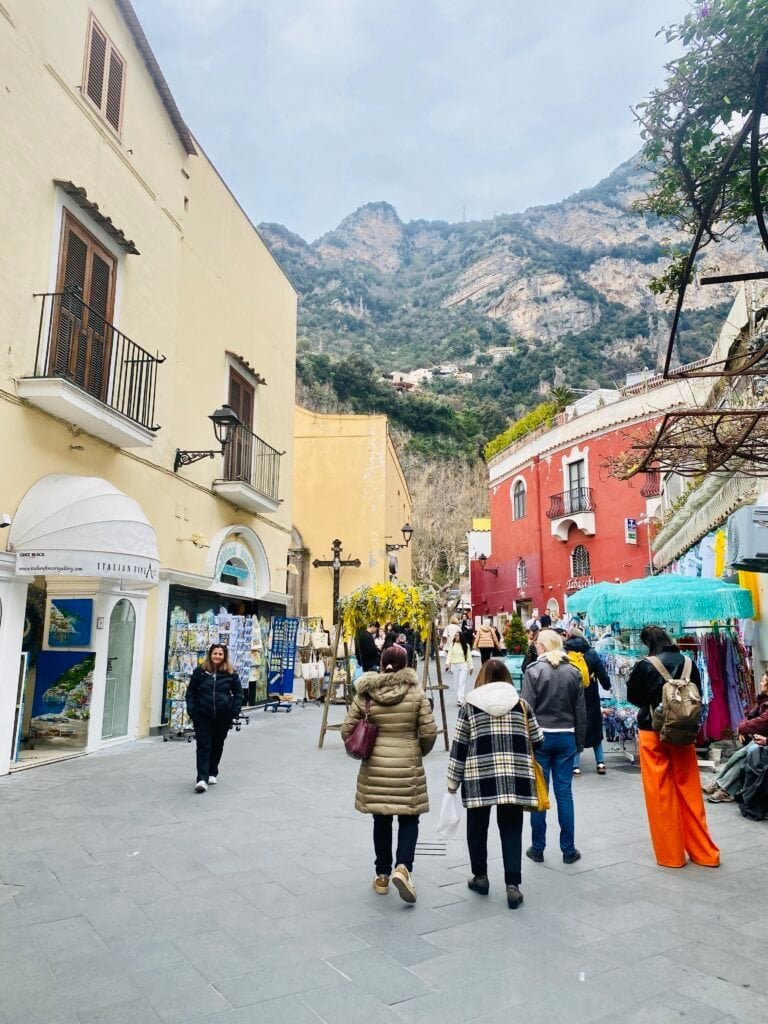 Vibrant street scene in Amalfi, Italy, showcasing colorful buildings, local shops, and tourists exploring the charming coastal town with mountainous backdrop.