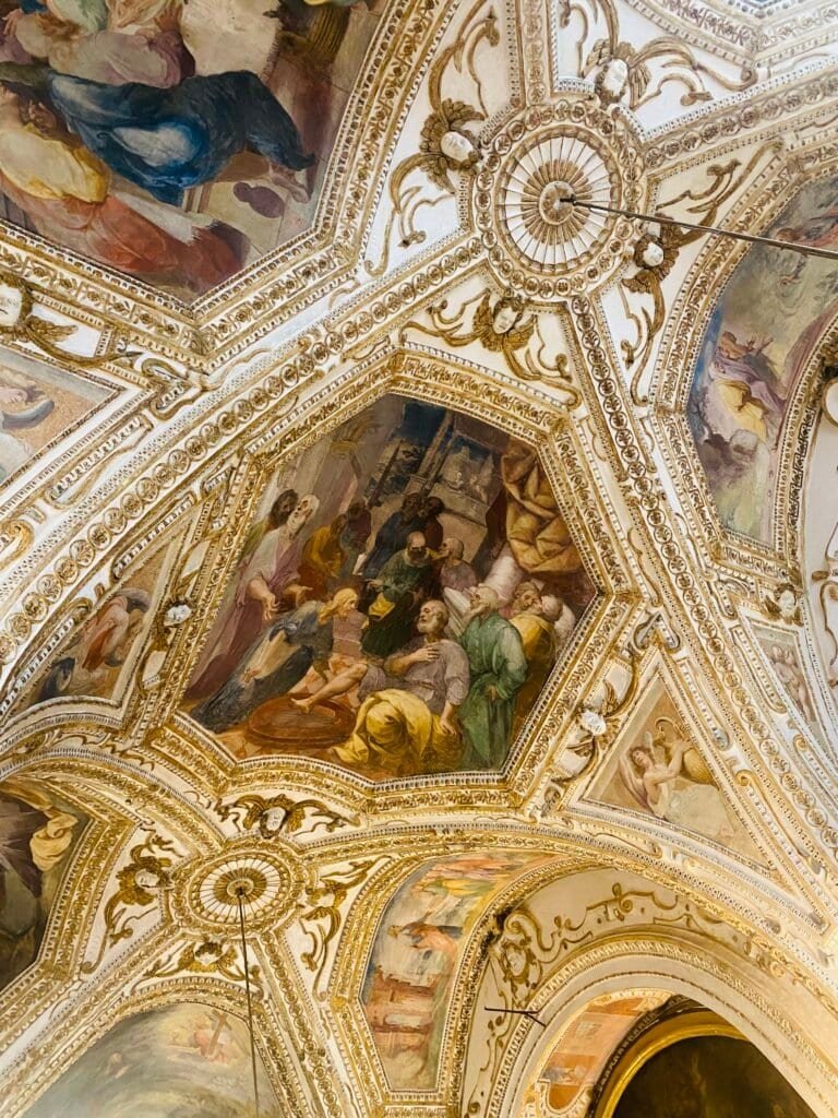 Intricate ceiling artwork featuring religious scenes and elaborate gold accents in a historic Italian church interior.
