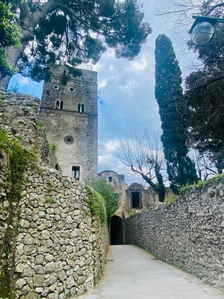 Historic stone castle with a tower surrounded by trees and stone walls in Italy, under a partly cloudy sky.