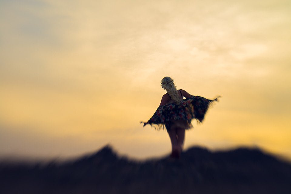 A woman standing on a hill at sunset, wearing a colorful dress, with her arms outstretched and hair flowing in the breeze.