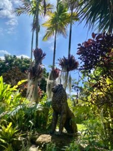 Lion sculpture amidst tropical plants and palm trees in a vibrant garden scene.
