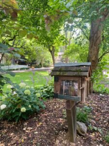 Wooden birdhouse on a post surrounded by lush greenery and blooming hydrangeas in a peaceful garden setting.