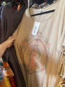 A vintage-style T-shirt featuring a religious image, hanging among other clothing items in a store.