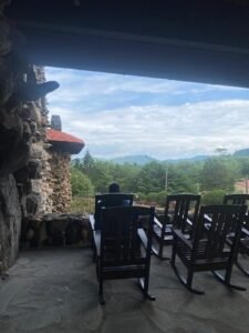 Chairs on a porch overlooking lush green landscape and distant mountains under a partly cloudy sky.