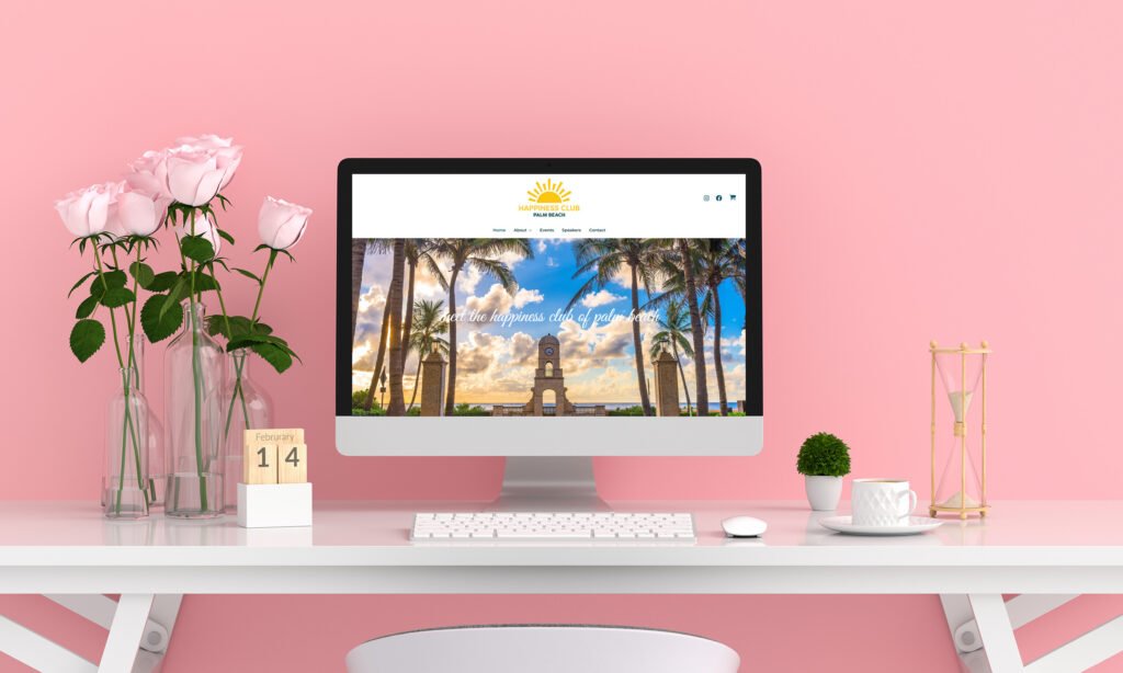 A modern workspace with a pink wall, a white desk, and a computer displaying a website with a tropical scene.