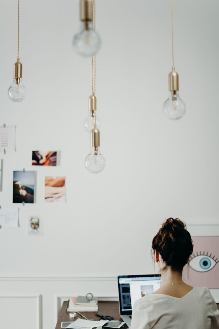 pexels-photo-3585034-3585034 Woman working at a desk in a modern creative office, surrounded by mood boards and hanging lightbulbs.
