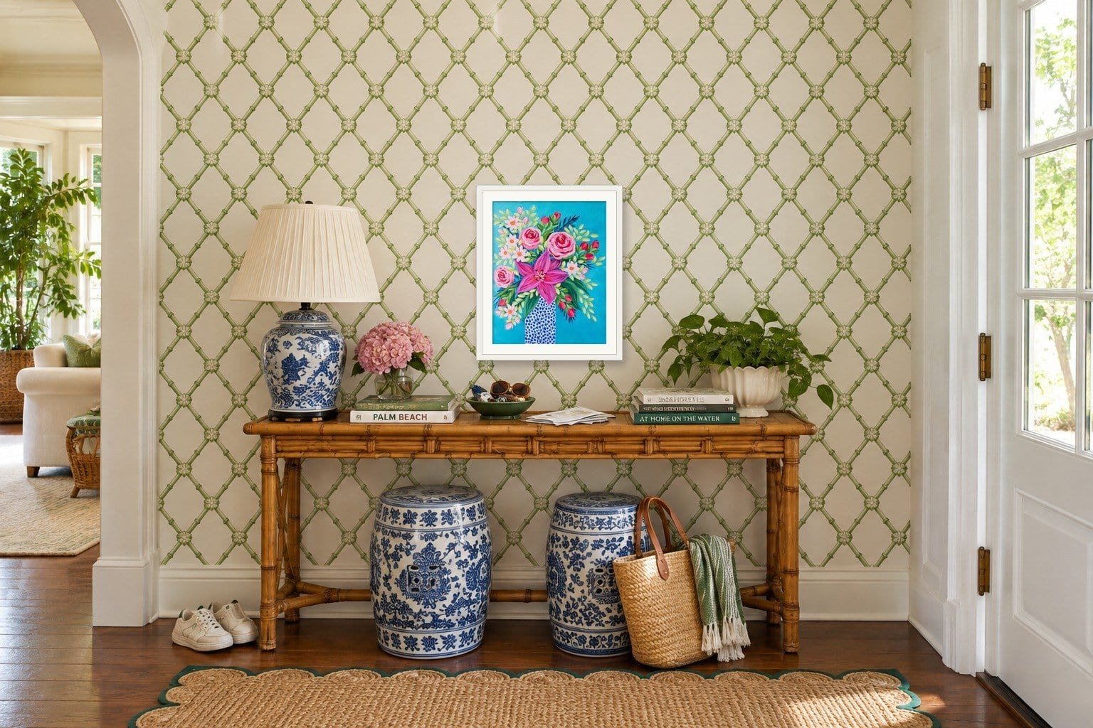 Entryway art: a framed floral painting by Bonnie Sorsby centered over a faux bamboo console with a ginger jar lamp, blue and white garden stools and green lattice wallpaper